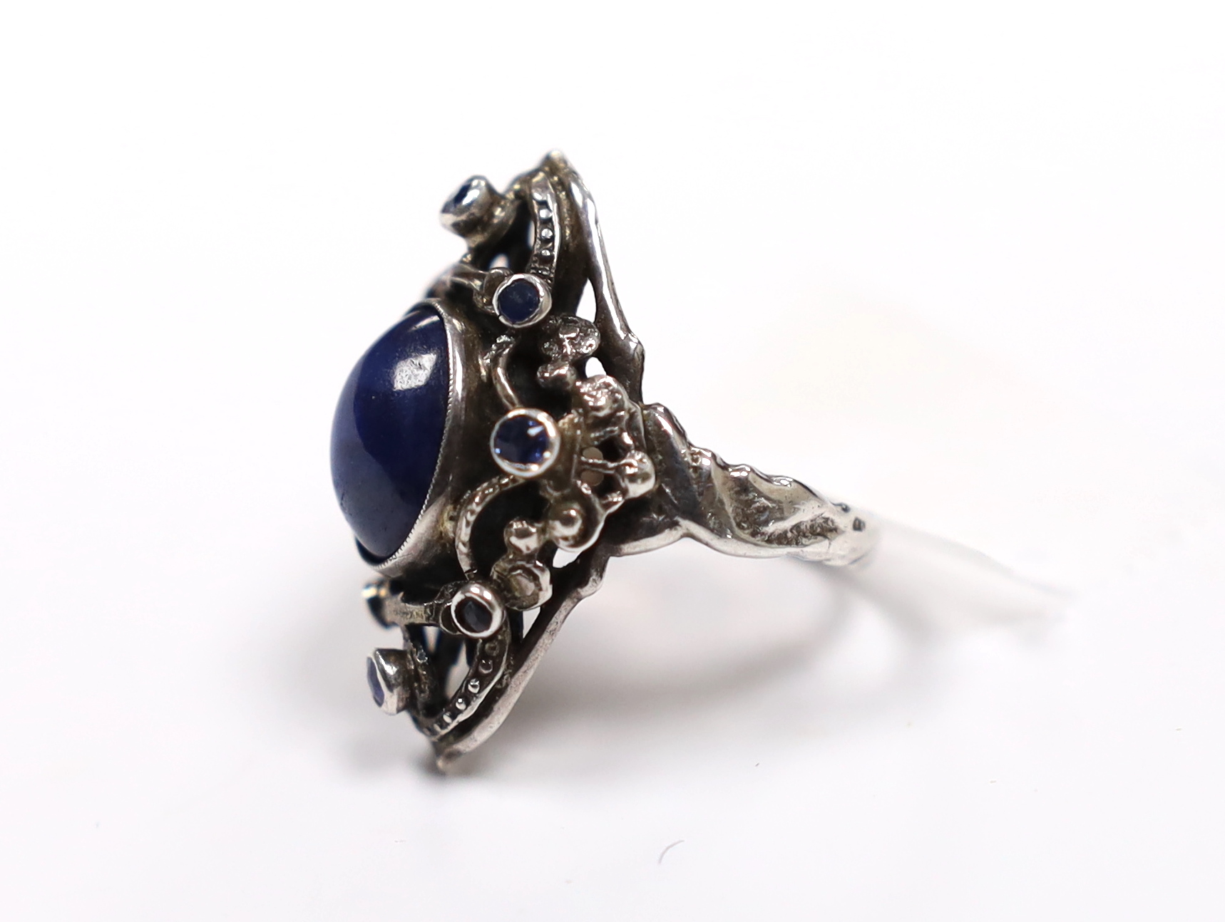 An Arts & Crafts pierced white metal and blue cabochon set dress ring, bordered with seven (ex 8) blue stones, size M.